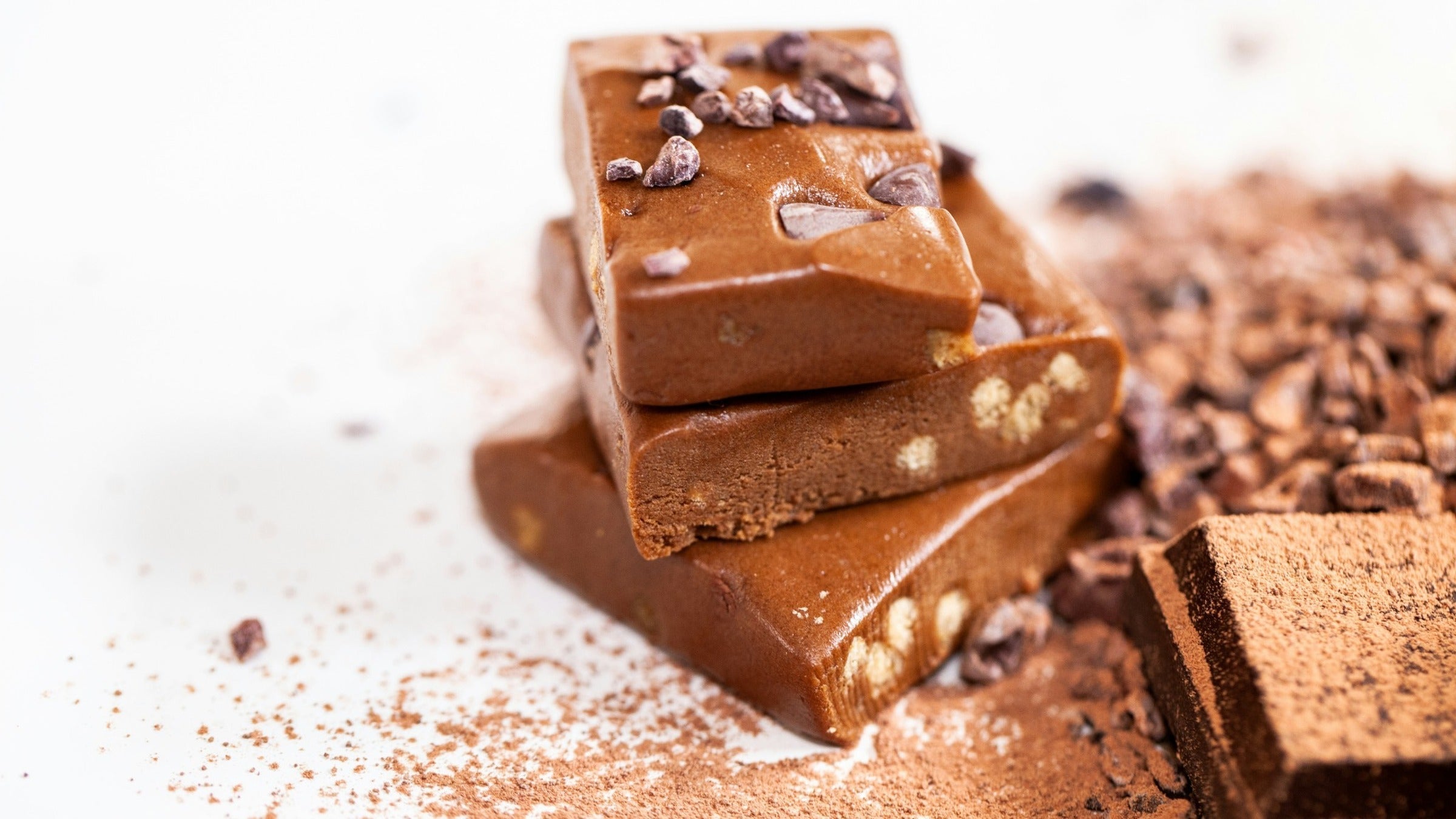 Stack of chocolate protein bar pieces with cacao nibs and cocoa powder on a white surface