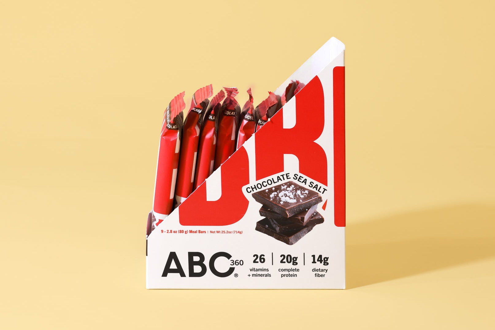 A display box of ABC360BAR.COM Chocolate Sea Salt protein bars on a beige surface, highlighting 26 vitamins & minerals, 20g complete protein, 14g fiber, and marine collagen. Several individually wrapped bars are shown.