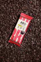 A wrapped ABC360BAR.COM Chocolate Sea Salt protein bar with marine collagen rests on chocolate chips; its red and beige packaging displays bold branding and nutrition highlights, emphasizing the healthy benefits of this meal bar.