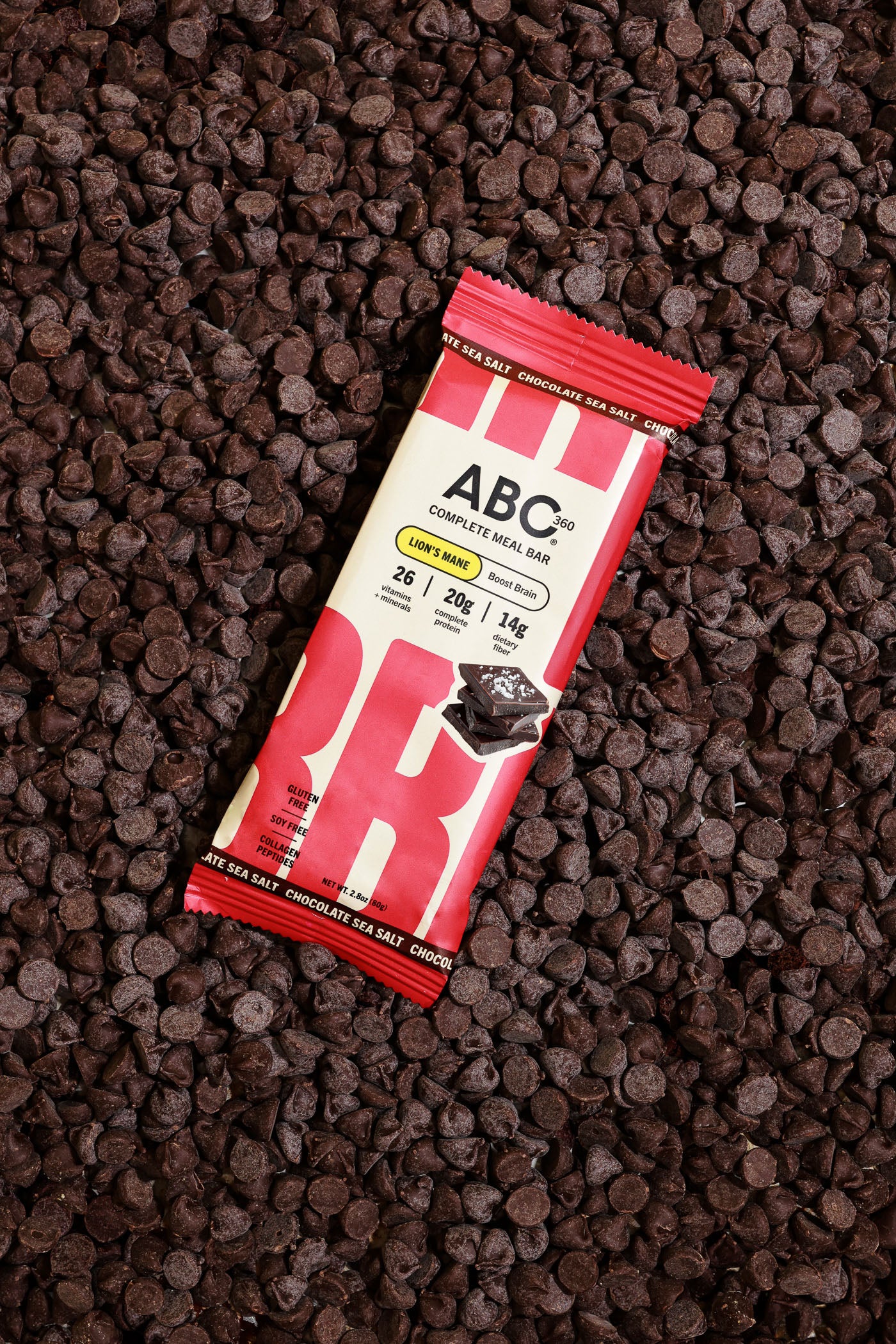 A wrapped ABC360BAR.COM Chocolate Sea Salt protein bar with marine collagen rests on chocolate chips; its red and beige packaging displays bold branding and nutrition highlights, emphasizing the healthy benefits of this meal bar.
