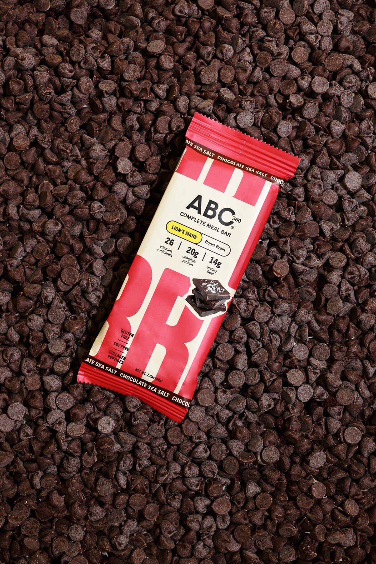 A wrapped ABC360BAR.COM Chocolate Sea Salt protein bar with marine collagen rests on chocolate chips; its red and beige packaging displays bold branding and nutrition highlights, emphasizing the healthy benefits of this meal bar.